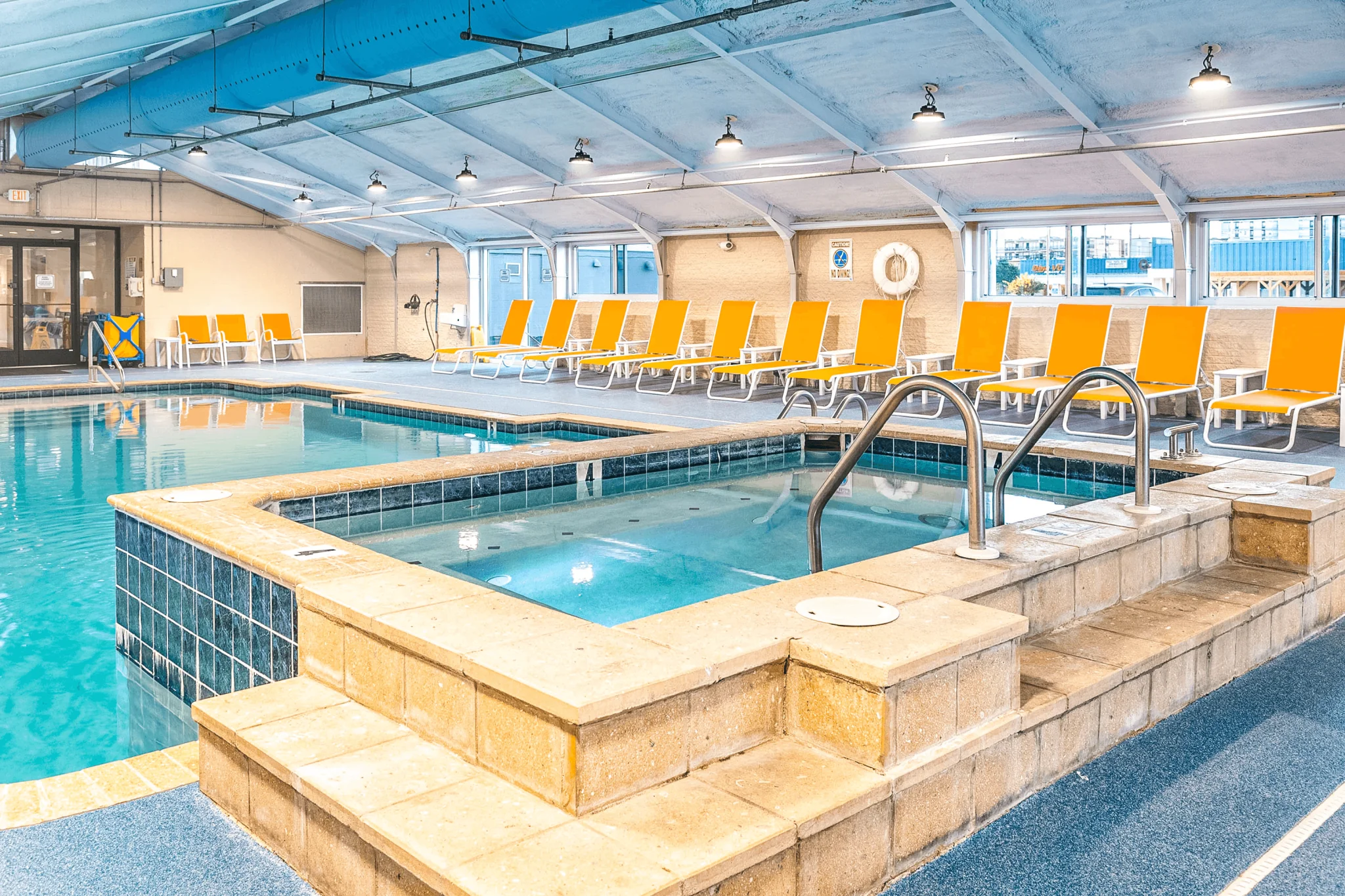 An indoor pool with a hot tub and lounge chairs.